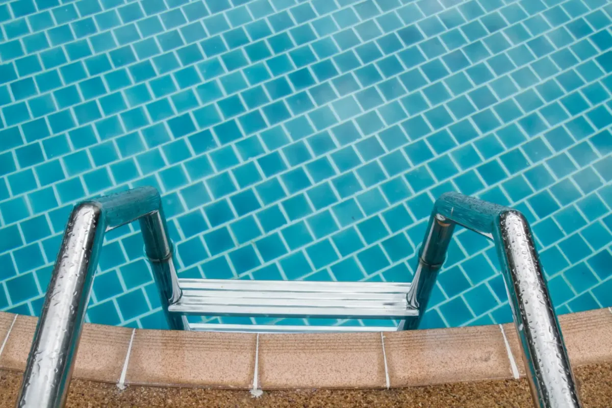 Escalera de acero inoxidable sobre el gresite turquesa de una piscina, con las juntas limpias